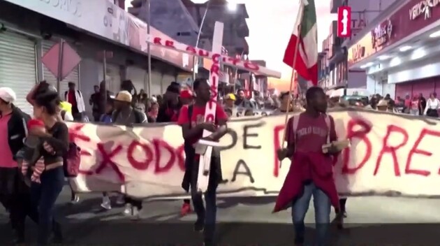 Впереди каравана мигранты несут баннер с надписью «Бегство от бедности»