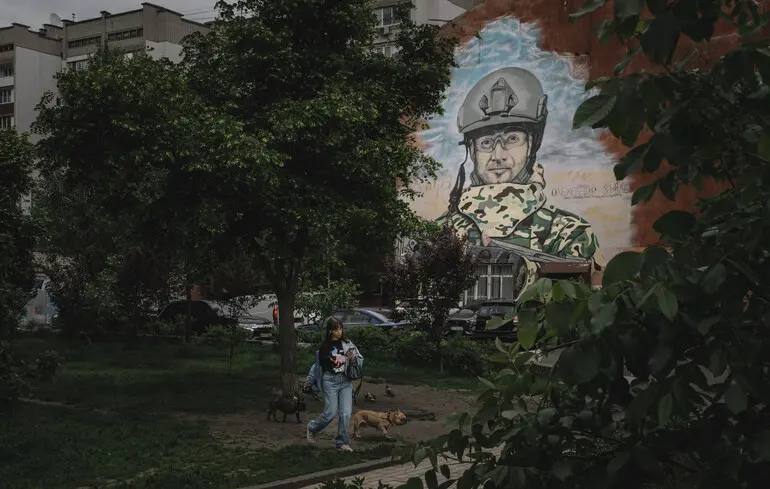 У Києві жінка йде перед муралом, присвяченим українському військовому та чемпіону з хокею Олександру Хмілю / 20 травня 2025 року