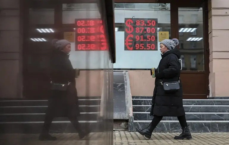 Жінка йде біля обмінного пункту з електронною панеллю, яка показує курси обміну валют відносно рубля, Москва, Росія / 19 березня 2025 року