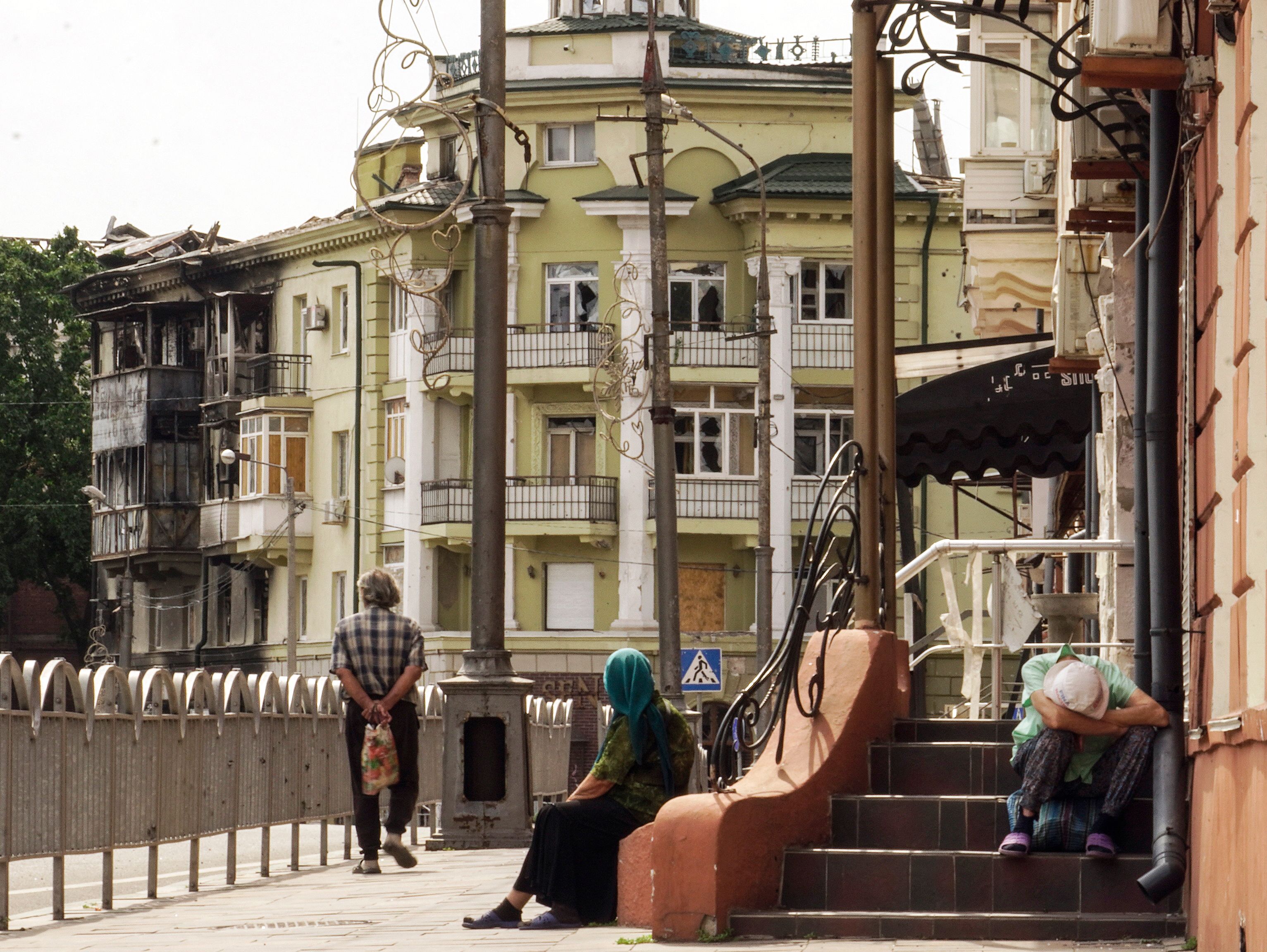Мешканці міста сидять перед зруйнованими будинками у Маріуполі 27 серпня 2022 року