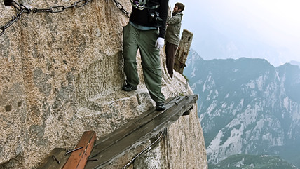 Путники ступают на приколоченные над бездной доски и двигаются к вершине в обнимку со скалой